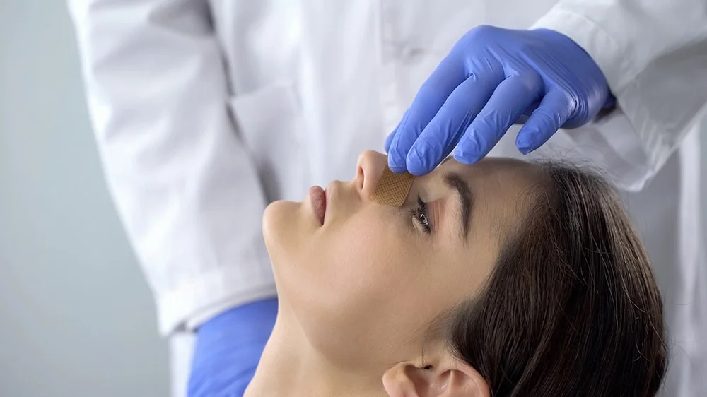 A doctor examining a bandage on a woman's nose